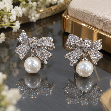 Silver-tone bow earrings with closely arranged clear accents, curved ribbon loops, notched tails and round ivory-white pearl-look drops.