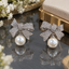 Silver-tone bow earrings with closely arranged clear accents, curved ribbon loops, notched tails and round ivory-white pearl-look drops.