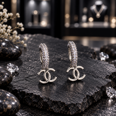 Pair of silver-tone rounded hoops with rows of clear-looking accents and smooth overlapping double-C hanging charms.