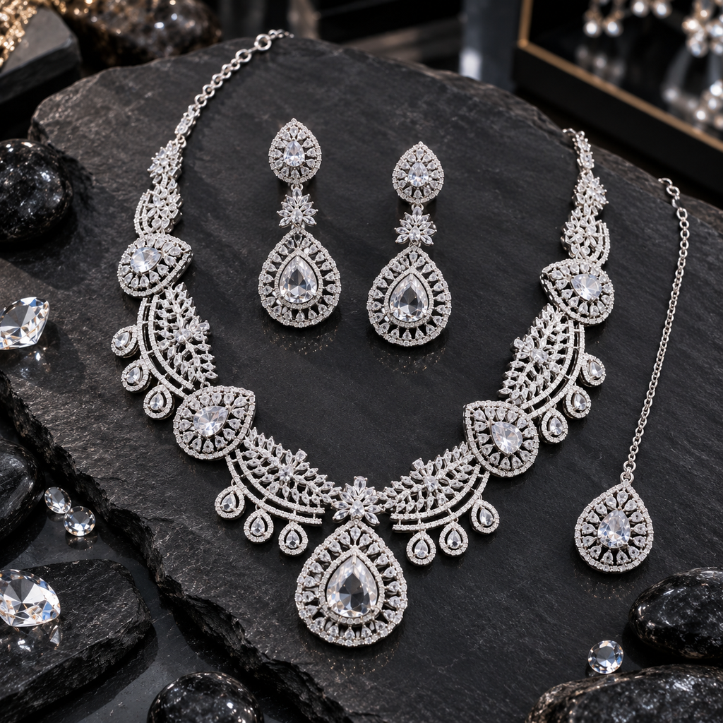 Silver-tone necklace with clear-looking teardrop motifs, leaf-filled curved fan sections and teardrop fringe, with matching floral-connector earrings and bindia.