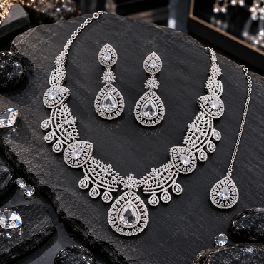 Silver-tone necklace with clear-looking teardrop motifs, leaf-filled curved fan sections and teardrop fringe, with matching floral-connector earrings and bindia.
