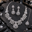 Silver-tone necklace with clear-looking teardrop motifs, leaf-filled curved fan sections and teardrop fringe, with matching floral-connector earrings and bindia.
