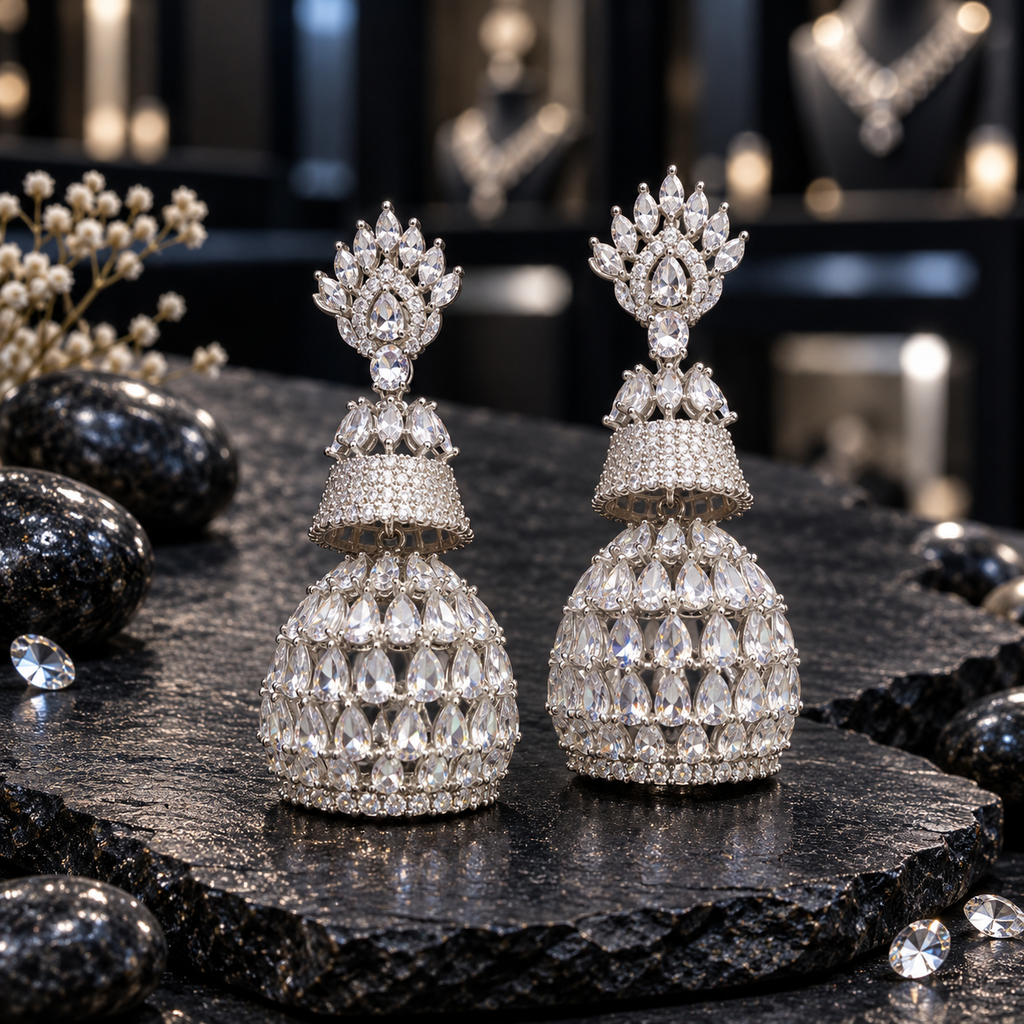 Pair of silver-tone tiered AD jhumka earrings with clear crown-like tops, sparkling upper bells and clear teardrop-covered lower domes.
