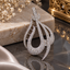 Silver-tone curved teardrop pendant with clear accents, sweeping asymmetric outlines, openwork crossbars and an elongated hanging loop.