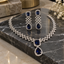 Silver-tone geometric necklace and matching drop earrings with dark blue rectangular and teardrop-shaped accents bordered by clear details.