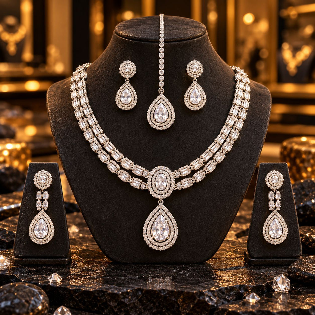 Silver-tone double-row necklace with an oval centre and clear teardrop pendant, long earrings on side stands and matching maang tikka; an additional short earring pair is displayed on the bust but is not included.