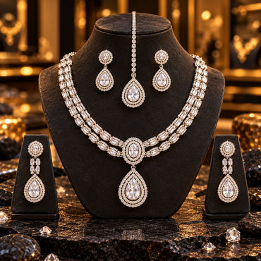 Silver-tone double-row necklace with an oval centre and clear teardrop pendant, long earrings on side stands and matching maang tikka; an additional short earring pair is displayed on the bust but is not included.
