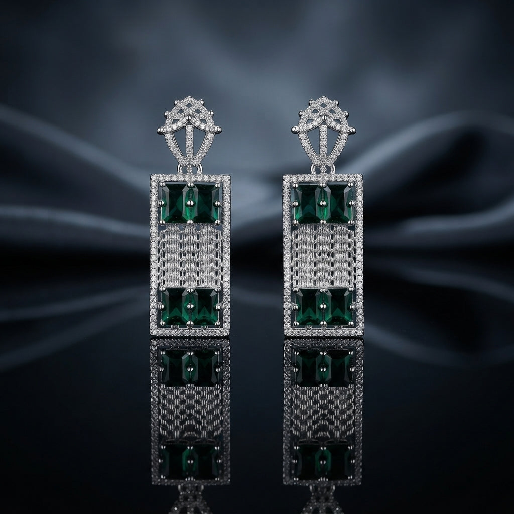 Silver-Tone Emerald CZ Rectangle Frame Mesh Drop Earrings displayed upright on dark grey mirror surface with dark blue silk drape backdrop showing pair of long rectangle drop earrings with open-work crown lantern filigree stud top in white CZ pave large rectangular open frame with white CZ pave border woven mesh grid center panel and two large emerald-cut emerald-green CZ stones in 4-prong settings at top and bottom with mirror reflection below