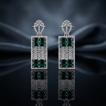 Silver-Tone Emerald CZ Rectangle Frame Mesh Drop Earrings displayed upright on dark grey mirror surface with dark blue silk drape backdrop showing pair of long rectangle drop earrings with open-work crown lantern filigree stud top in white CZ pave large rectangular open frame with white CZ pave border woven mesh grid center panel and two large emerald-cut emerald-green CZ stones in 4-prong settings at top and bottom with mirror reflection below