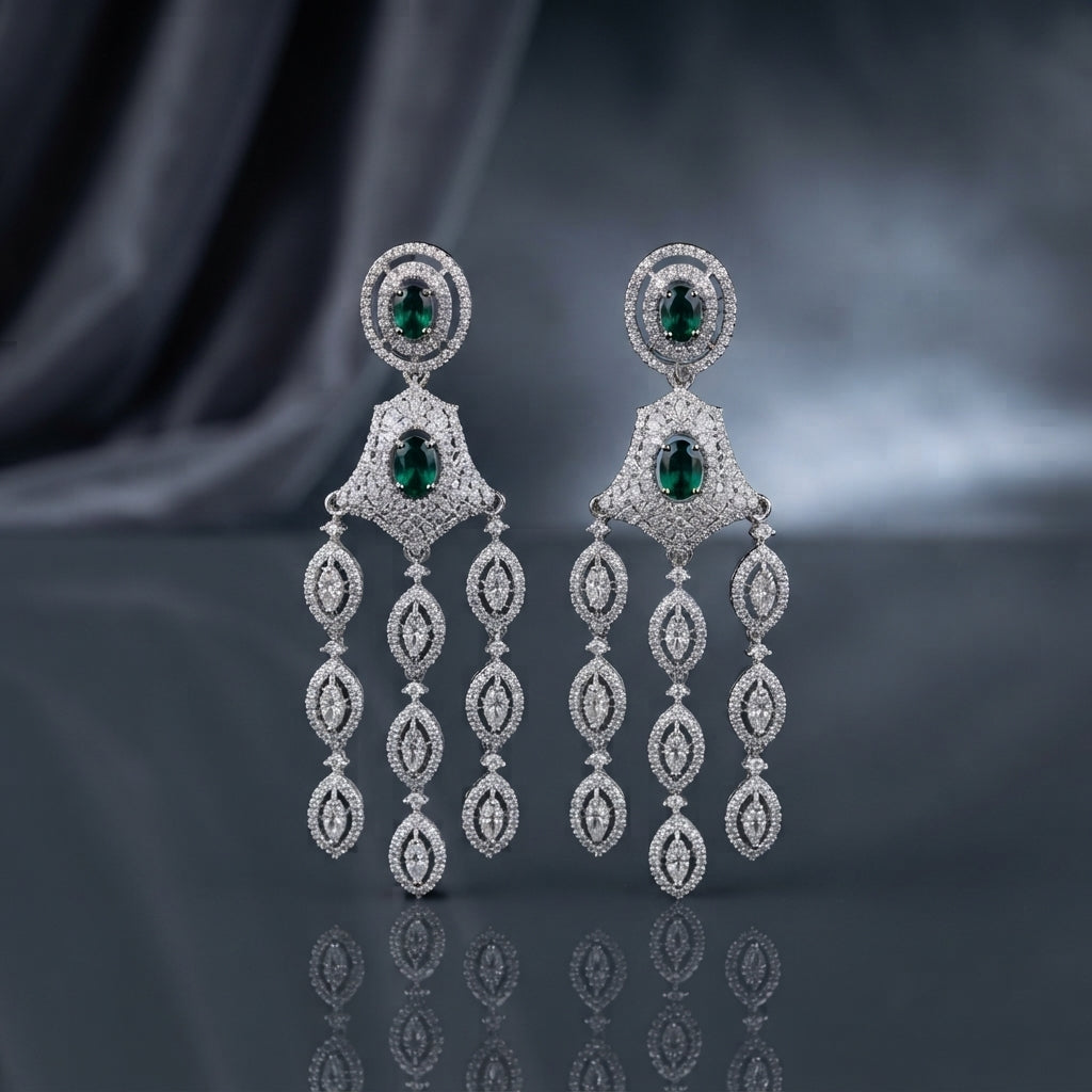 Silver-Tone Emerald Green Oval CZ Double Halo and Marquise Tassel Chandelier Earrings displayed upright on dark grey mirror surface with dark silk drape backdrop showing pair of extra-long chandelier tassel earrings with oval emerald-green CZ double concentric white CZ pave halo stud top diamond kite-shaped white CZ micro-pave panel with oval emerald CZ center and three cascading chains of four graduated marquise white CZ pave halo links with mirror reflection below