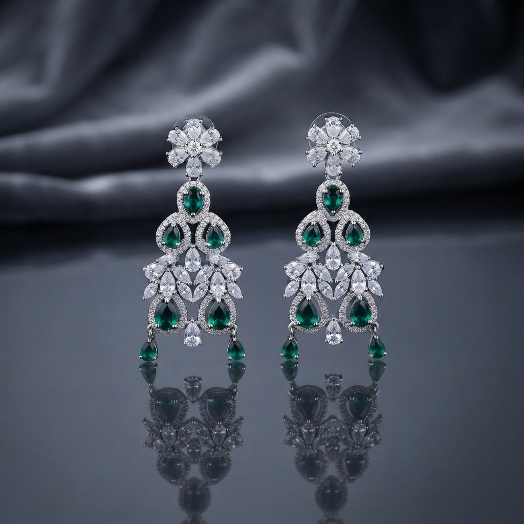 Silver-Tone Emerald Green and White CZ Floral Arch Chandelier Drop Earrings displayed upright on dark grey mirror surface with dark silk drape backdrop showing pair of long chandelier drop earrings with 6-petal marquise white CZ flower stud top arched double-ring frame with oval and pear emerald-green CZ fan spray of graduated marquise white CZ open arch lower frame with white CZ pave border and three pear emerald-green CZ dangles at base with mirror reflection below