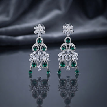 Silver-Tone Emerald Green and White CZ Floral Arch Chandelier Drop Earrings displayed upright on dark grey mirror surface with dark silk drape backdrop showing pair of long chandelier drop earrings with 6-petal marquise white CZ flower stud top arched double-ring frame with oval and pear emerald-green CZ fan spray of graduated marquise white CZ open arch lower frame with white CZ pave border and three pear emerald-green CZ dangles at base with mirror reflection below