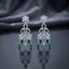 Silver-Tone Emerald Green and White CZ Floral Arch Chandelier Drop Earrings displayed upright on dark grey mirror surface with dark silk drape backdrop showing pair of long chandelier drop earrings with 6-petal marquise white CZ flower stud top arched double-ring frame with oval and pear emerald-green CZ fan spray of graduated marquise white CZ open arch lower frame with white CZ pave border and three pear emerald-green CZ dangles at base with mirror reflection below