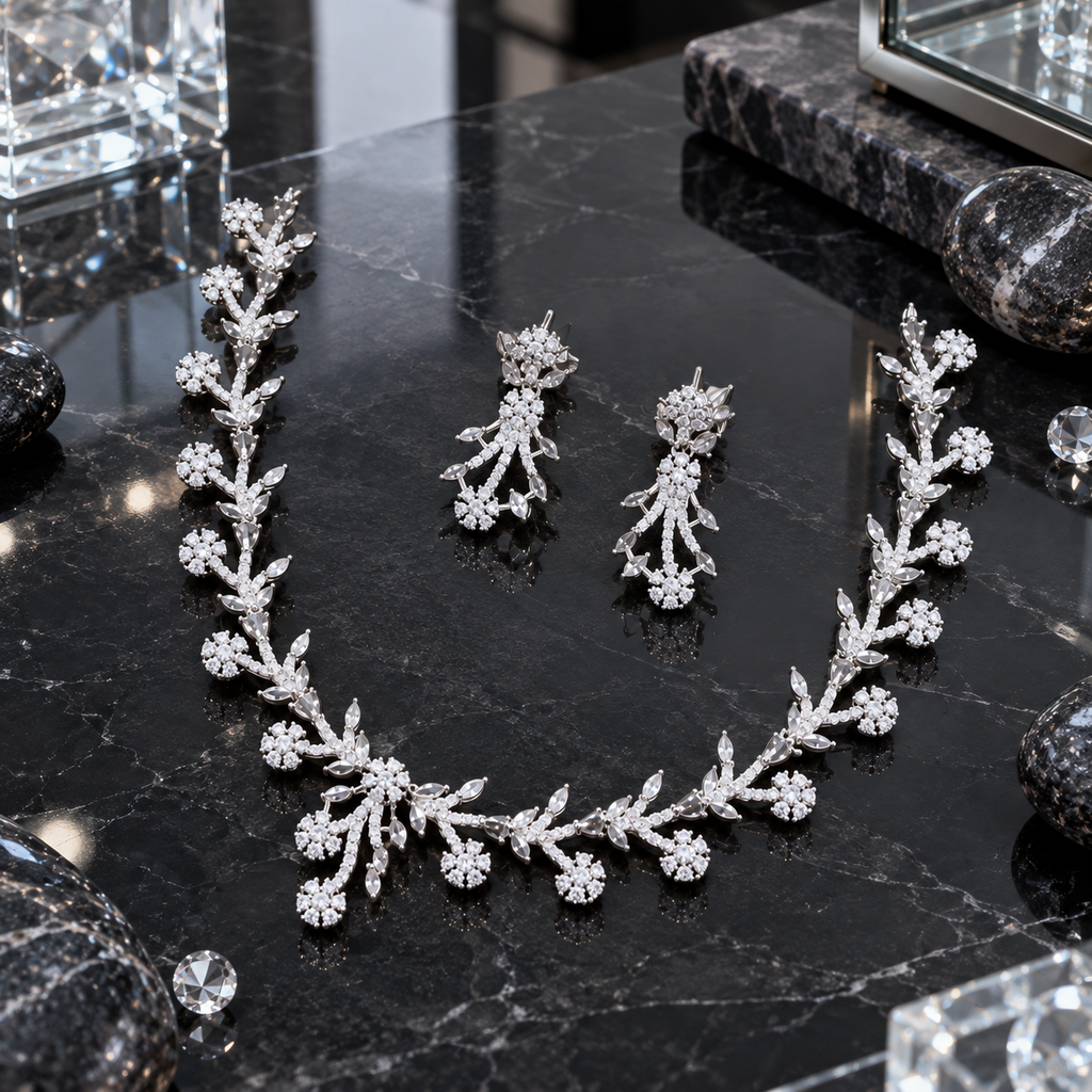 Silver-tone branching necklace and matching drop earrings with clear leaf-like accents, small flower clusters and an off-centre hanging necklace detail.