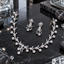 Silver-tone branching necklace and matching drop earrings with clear leaf-like accents, small flower clusters and an off-centre hanging necklace detail.