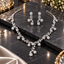 Silver-tone floral vine necklace and matching drop earrings with curved links, leaf-shaped details, clear accents, and flower-shaped drops.