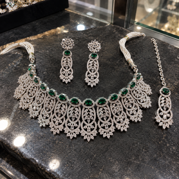 Silver-tone green American Diamond necklace, long earrings and chain-style bindia laid flat, with clear openwork panels, floral tips and white pearl-look side strands.