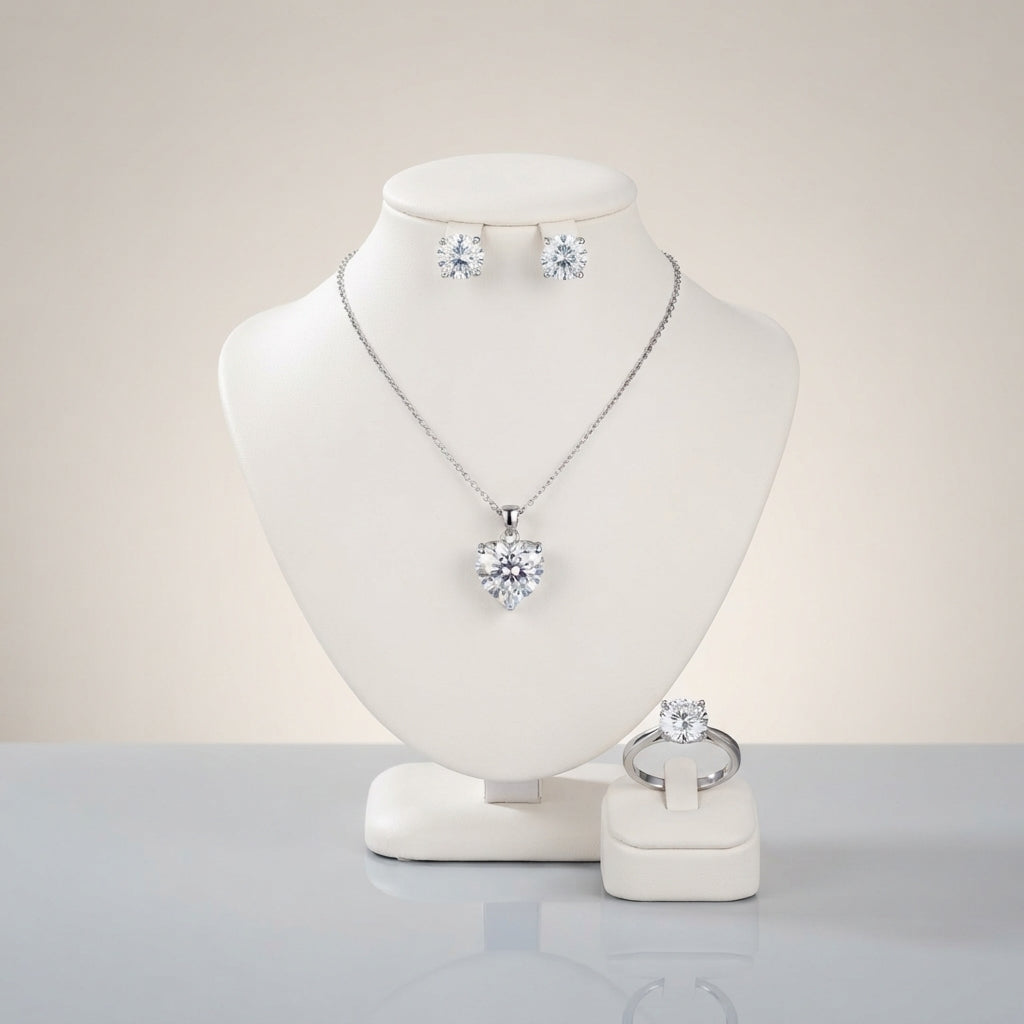 Silver-tone set displayed with a heart-shaped clear-looking pendant necklace, round stud earrings, and a matching ring.