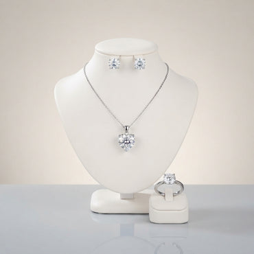 Silver-tone set displayed with a heart-shaped clear-looking pendant necklace, round stud earrings, and a matching ring.