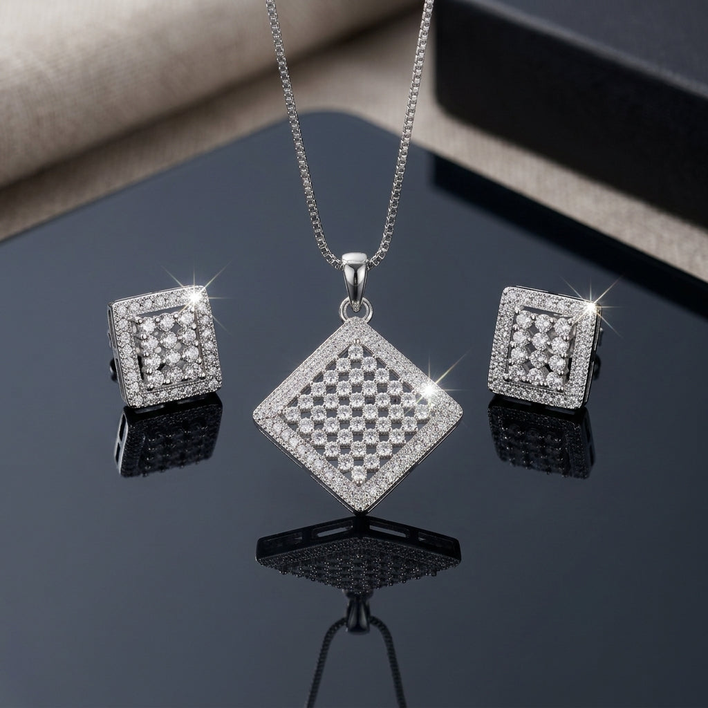 Silver-Tone Micro-Pavé CZ Diamond Checkerboard Pendant Necklace and Earrings Set flat lay on dark black mirror surface with grey leather backdrop showing large rhombus diamond shape pendant with checkerboard round CZ cluster grid and double micro-pave CZ border on silver box chain flanked by matching square stud earrings with mirror reflections below