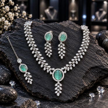Silver-tone necklace with a mint-green oval halo centre, paired clear-looking leaf details and a descending sprig, with matching earrings and bindia.