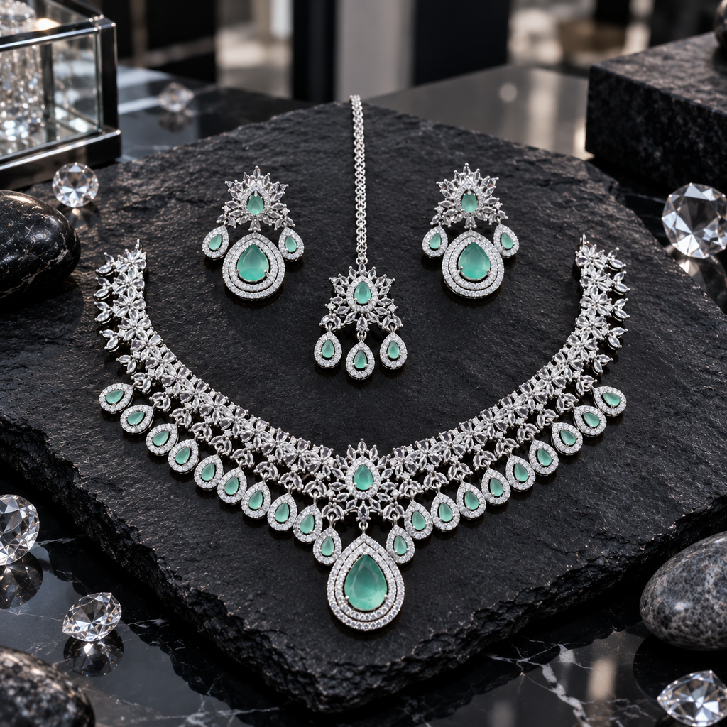 Silver-tone necklace, matching earrings and maang tikka with mint-green teardrop accents, clear floral details and a large teardrop necklace pendant.