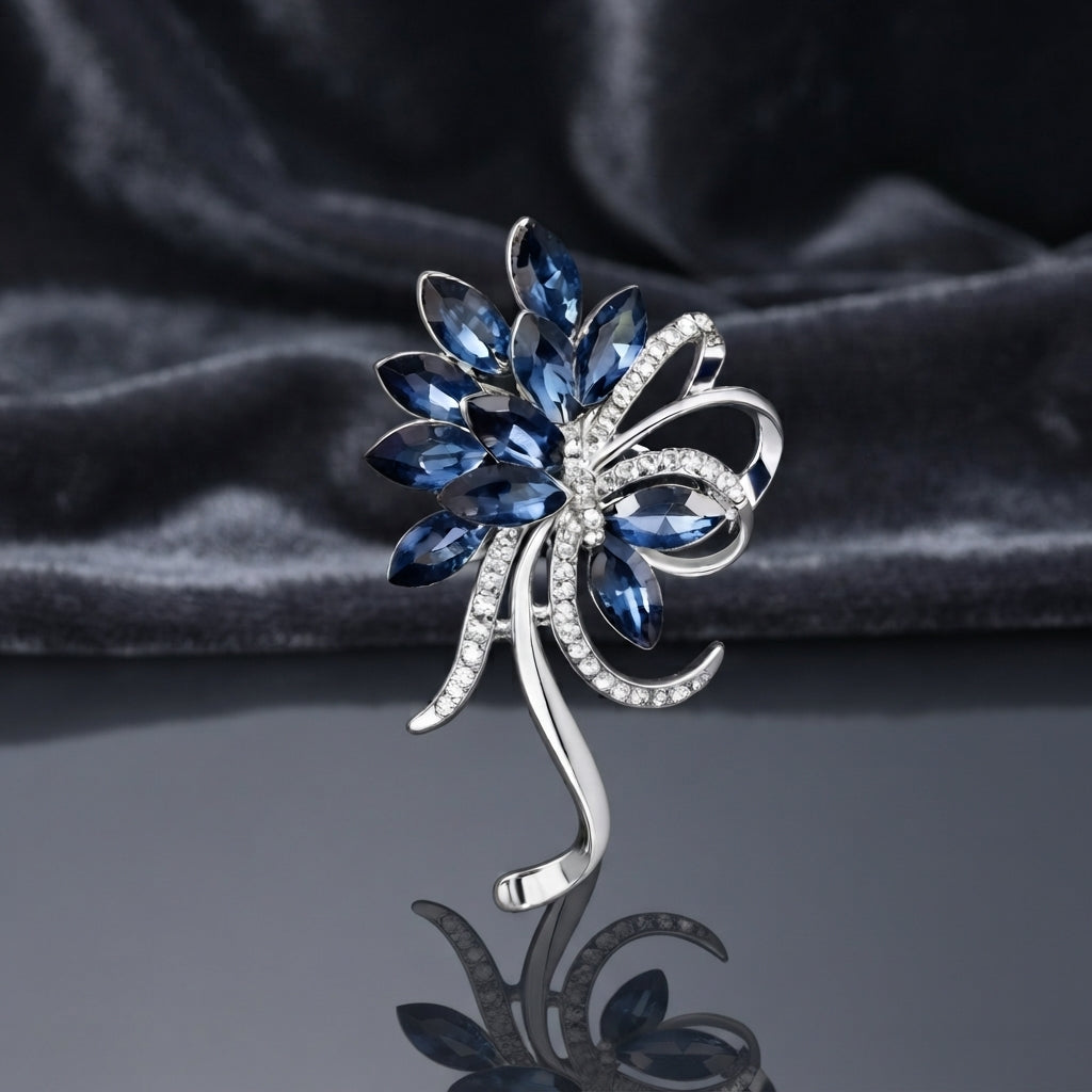 Silver-Tone Navy Blue Marquise Crystal Floral Spray Brooch Pin standing upright on dark grey mirror surface with dark grey silk backdrop showing sweeping fan of faceted marquise navy blue crystal petals and leaves with micro-pave CZ ribbon bow scroll center two navy blue marquise crystal accents and elongated silver curling scroll stem tail with mirror reflection below