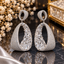 Silver-tone open teardrop drop earrings with oval tops, closely arranged small clear accents and larger rectangular and angular clear details.