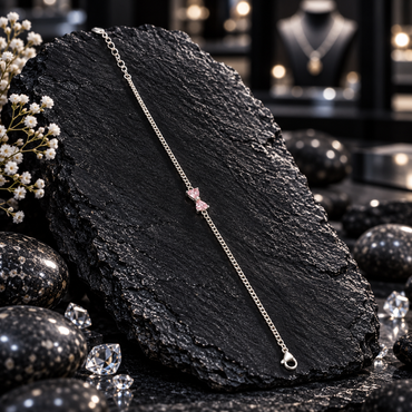 Single silver-tone fine chain payal anklet with two pale pink heart-shaped accents forming a small bow centre, a clasp and round-link tail.