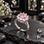 Silver-tone ring with a pink faceted centre surrounded by round clear-looking accents in a raised floral halo setting.