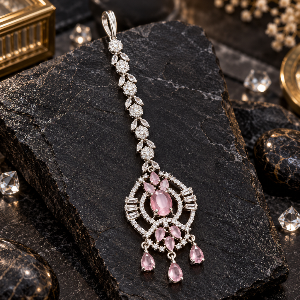 Silver-tone maang tikka with clear floral and leaf links, a pink oval centre, openwork circular borders and three pink teardrop-shaped hanging drops.