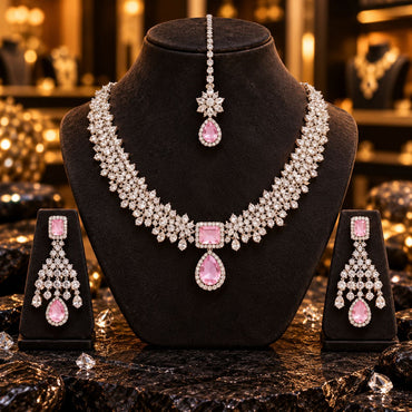 Silver-tone floral necklace with a square pink centre and pink teardrop pendant, matching pink chandelier earrings and floral maang tikka with a pink drop, displayed on dark stands.