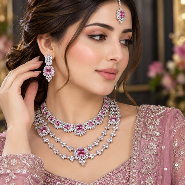 Model wearing a silver-tone layered necklace set with matching earrings and maang tikka, accented with pink details.