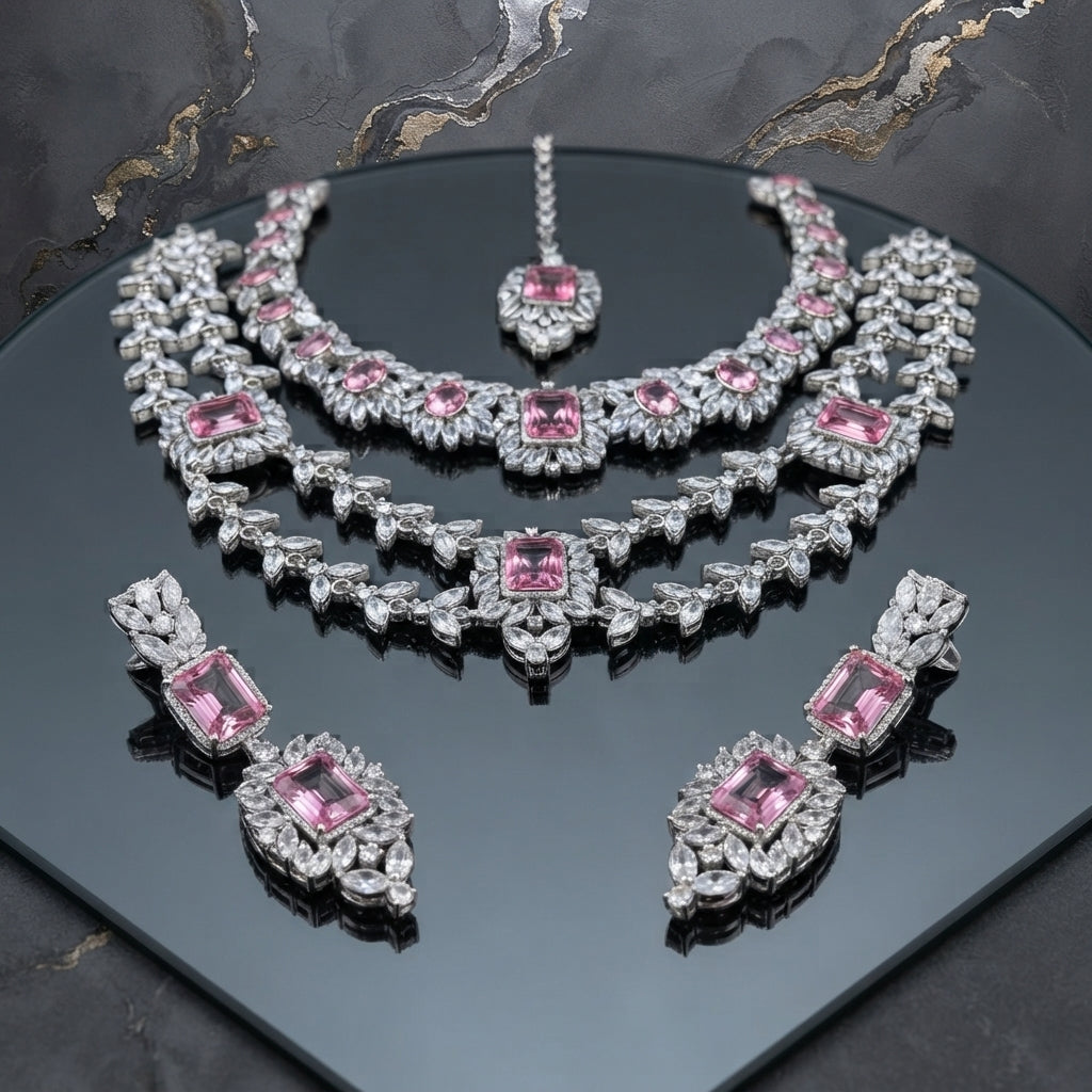 Silver-tone jewelry set with two necklaces, matching earrings, and maang tikka, accented with pink and clear faceted details.