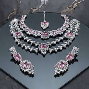 Silver-tone jewelry set with two necklaces, matching earrings, and maang tikka, accented with pink and clear faceted details.