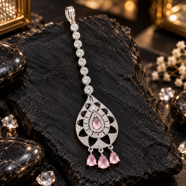 Silver-tone maang tikka with round clear links, a teardrop-shaped openwork frame, pink centre accent, rectangular clear border and three hanging pink drops.