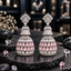 Pair of silver-tone tiered AD jhumka earrings with clear crown-like tops, sparkling upper bells and pink teardrop rows on the lower domes.