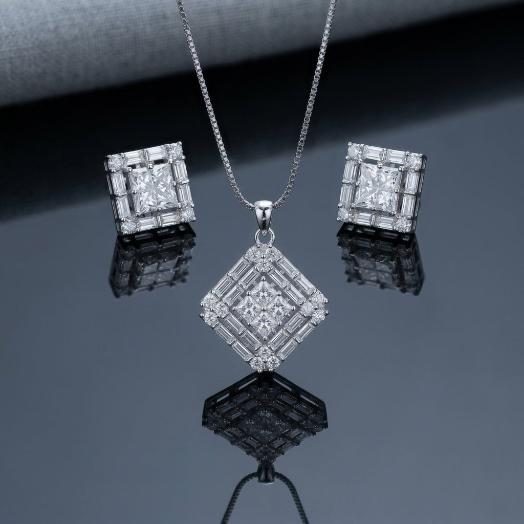 Silver-Tone Princess-Cut Baguette CZ Multi-Layer Diamond Pendant Necklace and Earrings Set flat lay on dark grey mirror surface with grey backdrop showing large rhombus diamond pendant with 4-stone princess-cut CZ quad cluster center inner baguette CZ channel ring and outer round micro-pave CZ halo on silver box chain flanked by matching square stud earrings with mirror reflections below