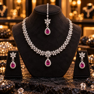 Silver-tone clear leaf necklace with a floral centre and pink teardrop framed by clear accents, matching pink halo drop earrings and floral maang tikka on dark stands.