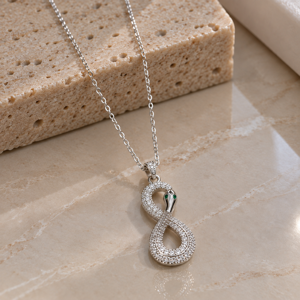 Silver-tone serpent pendant necklace with a vertical figure-eight body, clear accents, green eye details and a fine linked chain.
