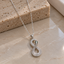 Silver-tone serpent pendant necklace with a vertical figure-eight body, clear accents, green eye details and a fine linked chain.