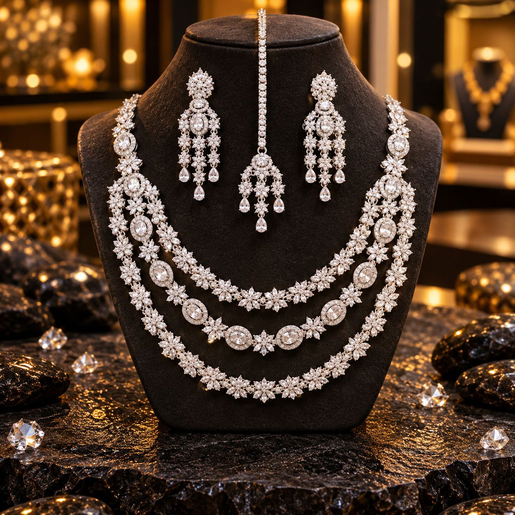 Silver-tone three-layer necklace with floral clusters and oval clear accents, matching chandelier earrings and a maang tikka with floral strands and teardrop drops, displayed on a dark bust.