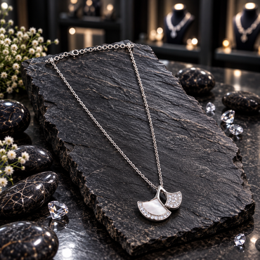 Silver-tone chain necklace with overlapping twin fan-shaped pendant sections, a white inset, clear accents and an open leaf-shaped detail, displayed on dark slate.