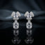 Silver-Tone White CZ Cushion Dome and Emerald-Cut Rectangle Halo Drop Earrings displayed upright on black mirror surface with dark grey silk drape backdrop showing pair of drop earrings with triple-petal trefoil dome cluster stud in round white CZ micro-pave with cushion princess-cut white CZ center in 4-prong setting oval CZ connector link and large emerald-cut rectangle white CZ drop with round white CZ pave halo border with mirror reflection below