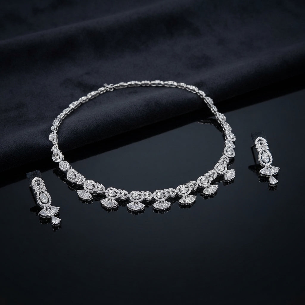 Silver White CZ Baguette Fan Leaf Necklace and Pear Drop Earrings Bridal Set — rhodium silver-tone 2-piece bridal set with continuous alternating baguette fan-leaf motif necklace with pear CZ centers flanking marquise CZ and radiating baguette fan drops and matching open marquise leaf stud with large pear CZ drop earrings displayed on dark black satin surface with mirror reflection