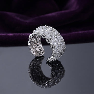 Silver White CZ Marquise Floral Cluster Open Cuff Wide Band Statement Ring top angled view on dark black mirror surface with deep purple velvet backdrop showing full wide band face with 6 to 8 tightly clustered 3D marquise-petal flowers and dense micro-pave white CZ fill across full circumference in rhodium silver with mirror reflection below