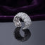 Silver White CZ Marquise Floral Cluster Open Cuff Wide Band Statement Ring top angled view on dark black mirror surface with deep purple velvet backdrop showing full wide band face with 6 to 8 tightly clustered 3D marquise-petal flowers and dense micro-pave white CZ fill across full circumference in rhodium silver with mirror reflection below