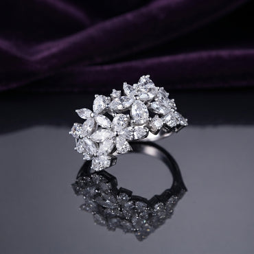 Silver White CZ Marquise Multi-Flower Cluster Wide Band Statement Ring front face view on dark grey mirror surface with deep purple amethyst velvet backdrop showing full wide band width with three 3D sculptural marquise-petal flower clusters pear accent stones and round white CZ fill in rhodium silver with full mirror reflection below