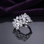 Silver White CZ Marquise Multi-Flower Cluster Wide Band Statement Ring front face view on dark grey mirror surface with deep purple amethyst velvet backdrop showing full wide band width with three 3D sculptural marquise-petal flower clusters pear accent stones and round white CZ fill in rhodium silver with full mirror reflection below