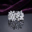 Silver White CZ Marquise Multi-Flower Cluster Wide Band Statement Ring angled top view on dark grey mirror surface with deep purple amethyst velvet backdrop showing three large 3D sculptural marquise-petal flowers with pear and round white CZ accents across full band in rhodium silver with full mirror reflection below